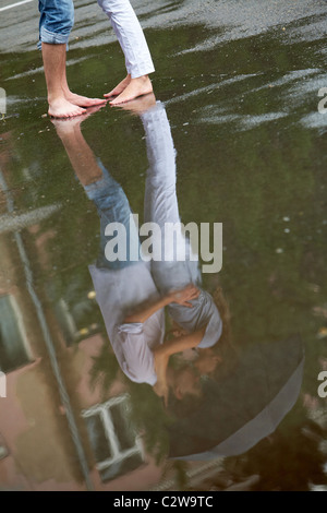 Reflection in puddle of woman and man embracing under umbrella during rain Stock Photo