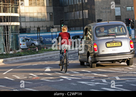 A female cyclist cycling around a roundabout next to a taxi in London England Stock Photo