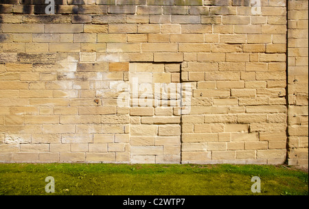 side on shot of stone wall with green grass. Wall seems to show door way, but door way bricked up shot on bright sunny day Stock Photo