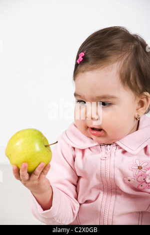 Amazed baby girl 11 months old holding a green apple in her hand and looking amazed to fruit Stock Photo