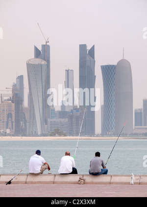 Men fishing  on The Corniche with modern office towers and skyline in business district in Doha Qatar Stock Photo