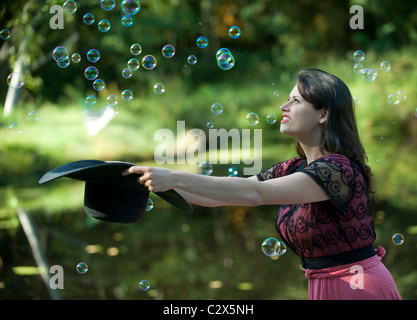 Caucasian woman trying to catch bubbles in hat Stock Photo