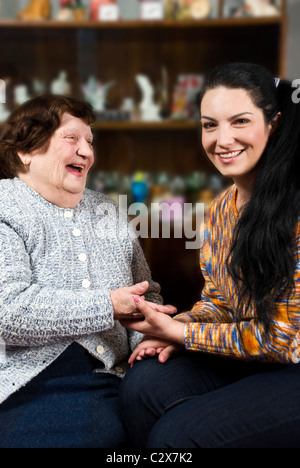 Grandmother 80s and her granddaughter 30s having a funny conversation and laughing together in living room,sitting on chairs and Stock Photo