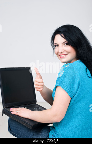 Happy woman sitting on white wooden floor using laptop blank screen and giving thumbs up ,rear view Stock Photo