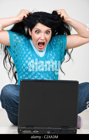 Furious woman screaming and tearing out her hair while using laptop Stock Photo