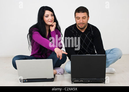 Young couple using laptops and sitting on laminate floor with legs crossed ,the woman pointing something on her husband laptop Stock Photo