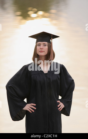 confident female college graduate with hands on hip with water background Stock Photo