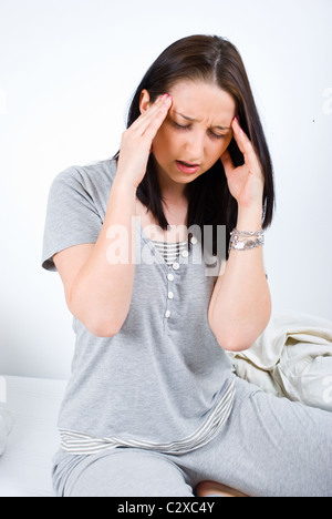 Woman sitting on bed and having a painful head ache Stock Photo