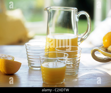 Glass jug and beakers filled with orange juice on wooden table top Stock Photo