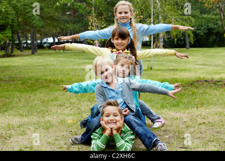 Portrait of happy friends lying on ground in park with stretched arms Stock Photo