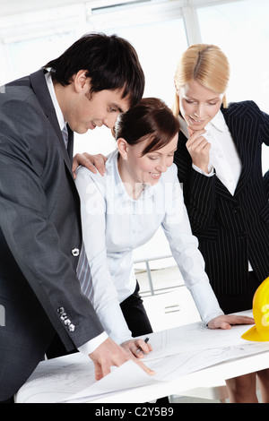 Three businesspeople bending over construction plan Stock Photo