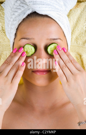 Beautiful young woman holding slices cucumber on her eyes at spa center Stock Photo