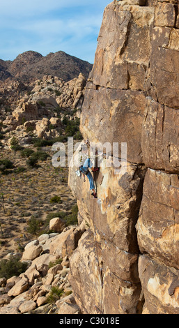 Female rock climber struggles for her next grip on the edge of a steep cliff. Stock Photo