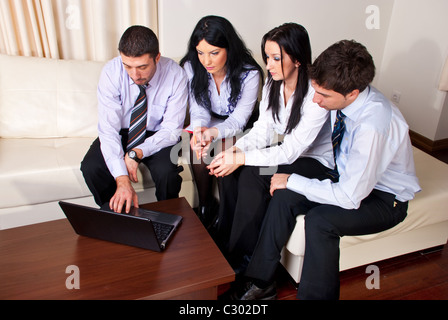 Four serious business people sitting on a couch n a office room and using laptop Stock Photo