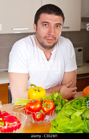 Mid adult man staring you and standing in kitchen with fresh vegetables on table Stock Photo