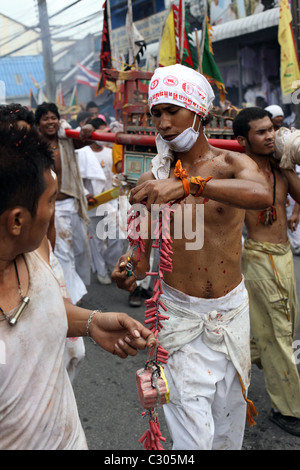 Young man lights fireworks during a street procession in the Phuket Vegetarian Festival. Phuket Town, Thailand Stock Photo