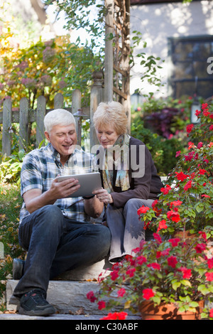 Happy mature couple sitting outside using a digital tablet Stock Photo