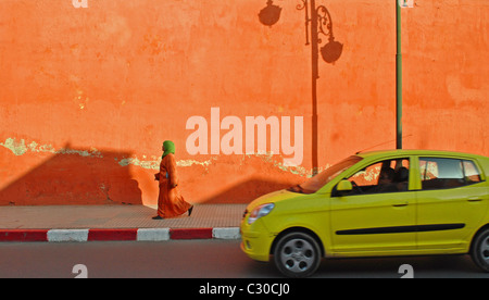A woman and car pass by the shadow of a lamp-post on a colourful wall in Marrakesh, Morocco Stock Photo