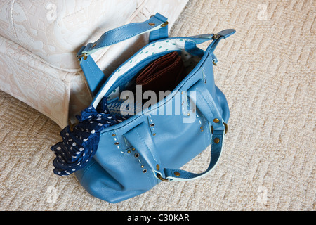 Women's blue leather handbag with zip open showing contents on the floor carpet beside a chair Stock Photo