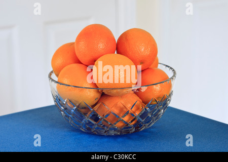 Fresh oranges in a crystal glass fruit bowl on a blue table. UK Stock Photo