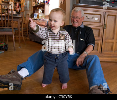 15 month old baby boy taking his first steps as his grandfather watches. Stock Photo