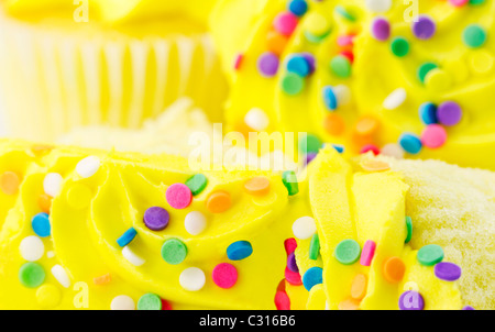Sliced vanilla cupcakes with sunny yellow frosting are in front of whole cupcakes in selective focus macro; close up. Stock Photo