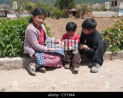 Three young Guatemalan children play on the side of a rural road near their home in Totonicapan, Guatemala. Stock Photo