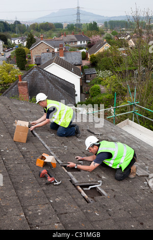 Men working on house roof in village fixing brackets for solar pv installation Wales UK Stock Photo