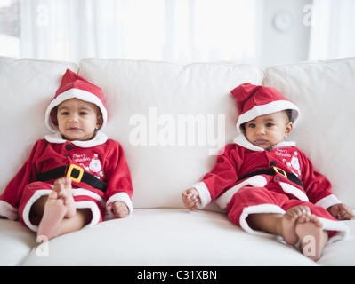 Twins on sofa dressed in Santa outfits Stock Photo