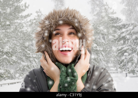 Mixed race woman in fur hood watching snow fall Stock Photo