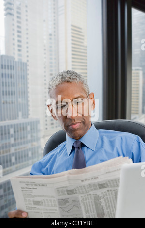 Mixed race businessman reading newspaper at desk Stock Photo