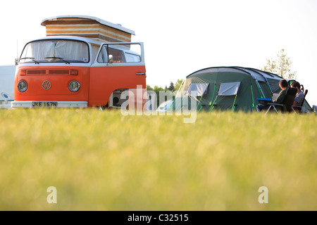 Couple sitting by tent and Volkswagen W camper van in a field in the morning light camping in East Sussex Stock Photo
