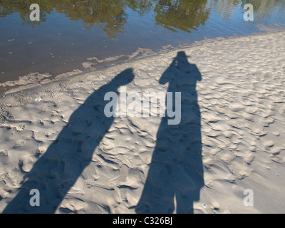 Shadows of two tourists exploring a pristine white sandy tropical island beach Stock Photo