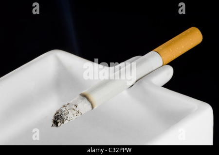 A burning cigarette in a white ashtray Stock Photo