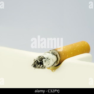 A burning cigarette in a white ashtray Stock Photo