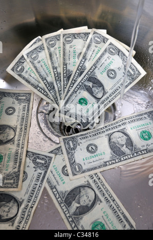 US dollars in a sink drain with water running concept good money going down the drain. Stock Photo