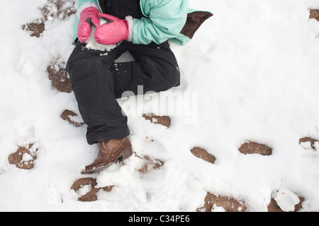 Girl making a snowball while sitting in the snow Stock Photo