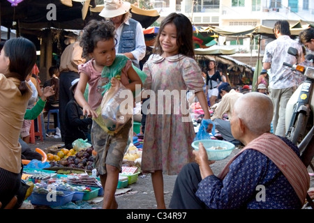 Two young street children girls are walking past an elderly woman begging for money in Phnom Penh, Cambodia. Stock Photo