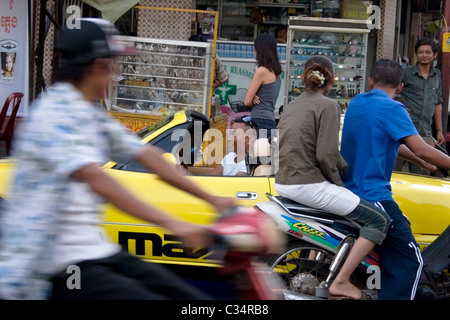 People riding motorcycles are looking at a man driving a convertable sportscar on a city street in Phnom Penh, Cambodia. Stock Photo