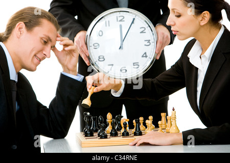 Image of businessman and businesswoman playing chess with businessman holding clock on background Stock Photo