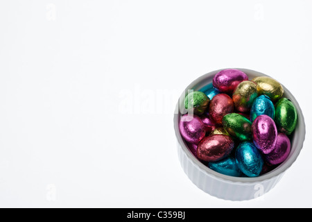 A bowl of tiny chocolate eggs, wrapped in multi-colored foil against a white background. Stock Photo