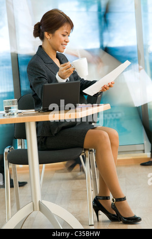 Photo of executive female looking through papers while having some coffee in office Stock Photo