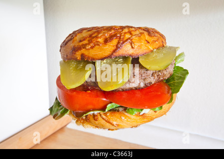 A hamburger on a cheese bagel with lettuce tomato and dill pickle Stock Photo