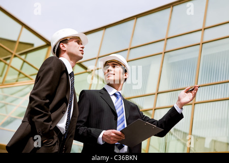 Photo of two co-workers discussing new project with modern building at background Stock Photo