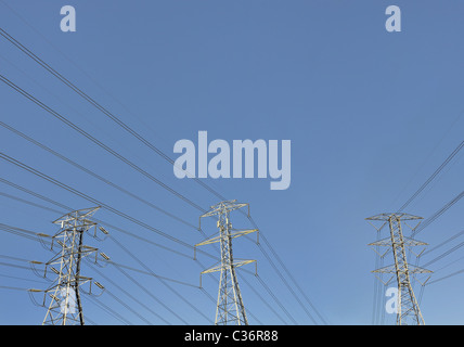 Electric wires on three tall metal transmission towers with electrical distribution power lines against a blue sky. Stock Photo