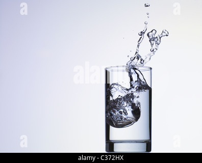 Cube of ice dropping into glass of water Stock Photo