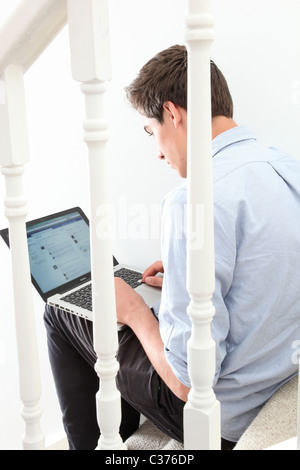 Young man using a laptop sitting on the stairs, facebook page open. Stock Photo