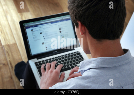 Over the shoulder shot of a young man using his laptop on a facebook page. Stock Photo