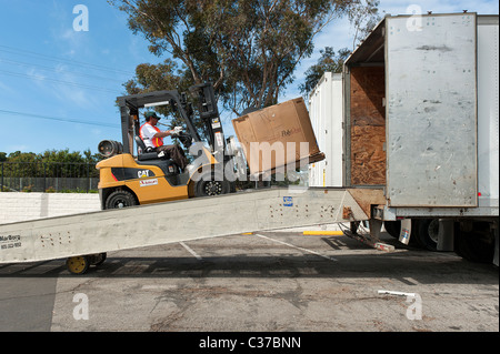 A forklift is loading a bin of e waste into a container of electronic waste for recycling in a collection center Stock Photo