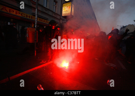 Demonstrators and policemen stand around red flare as violent clashes between Antifa extreme-left wing activists and police took place during protest rally on International Workers' Day, also known as Labour Day or May Day on 01 May in Kreuzberg district Berlin Germany Stock Photo